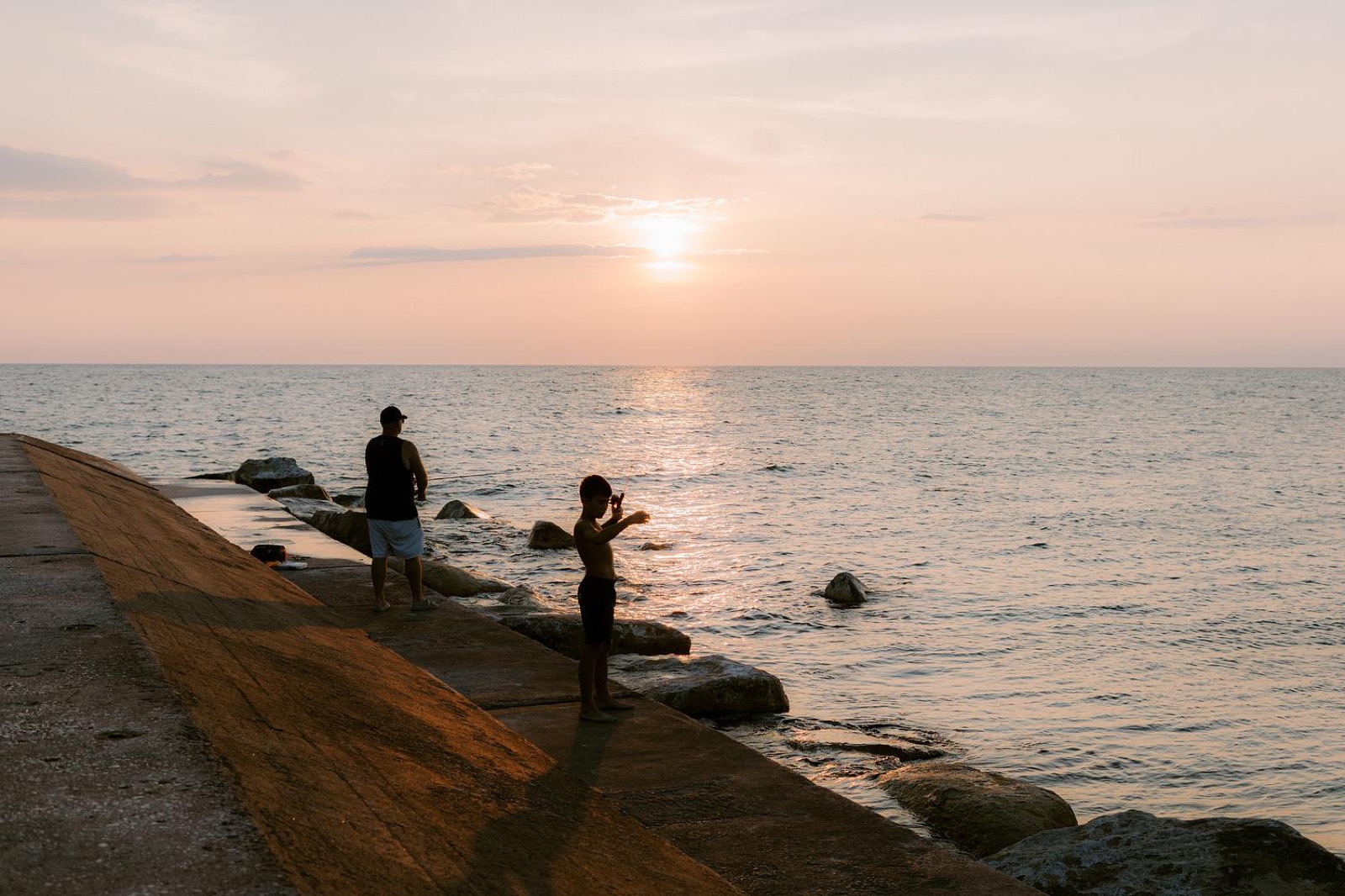 Two figures on a breakwater at sunset